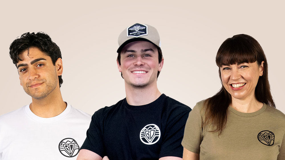 Three adults are photographed wearing Buckle-Down's new BD Logo T-shirts in different colors.