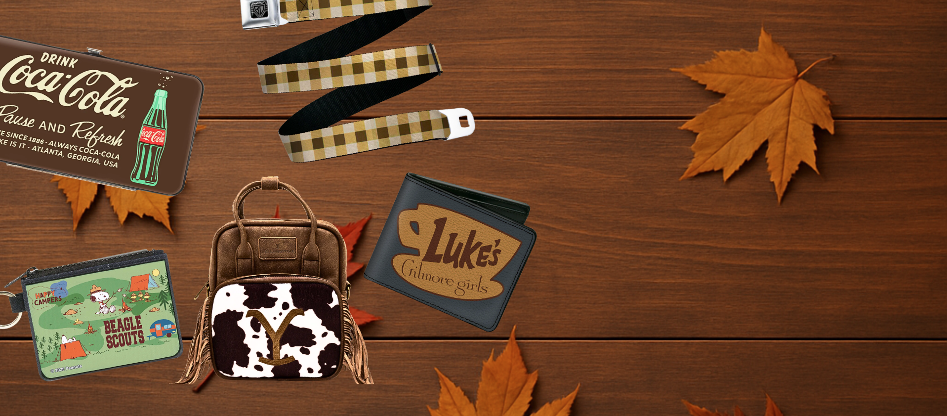 Collection of fall bags, plaid belt, coca cola and peanuts wallet on wooden floor with leaves featuring the brand "Buckle-Down"